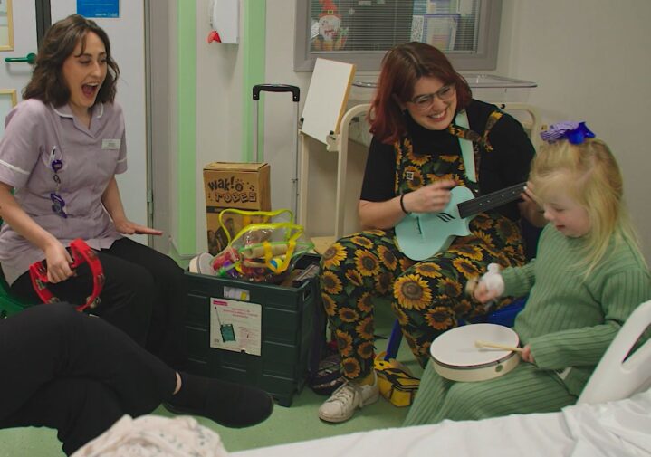 child plays drum supported by musician and hospital play specialist